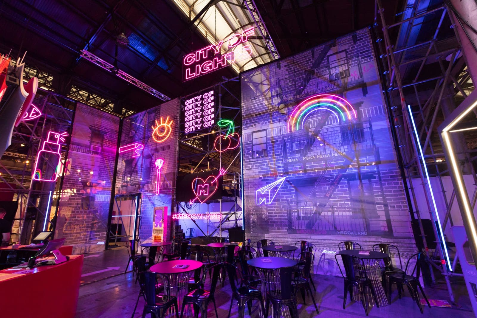The City of Lights zone: neon signs of beauty products, a heart and a rainbow on brick facades