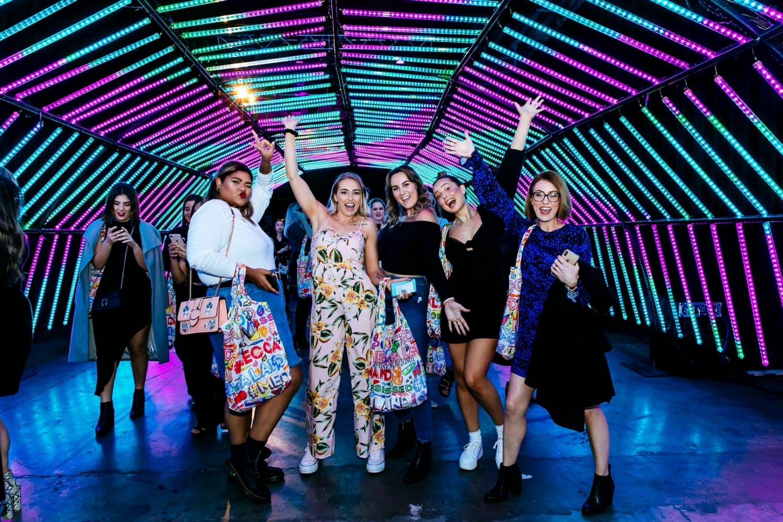 A group of friends cheer inside a tunnel of neon lights