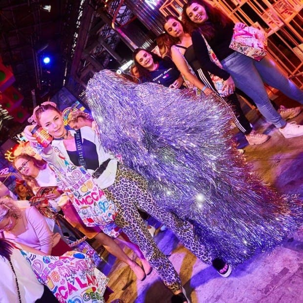 Festival-goers with MECCALAND tote bags crowd around a performer in a silver tinsel costume