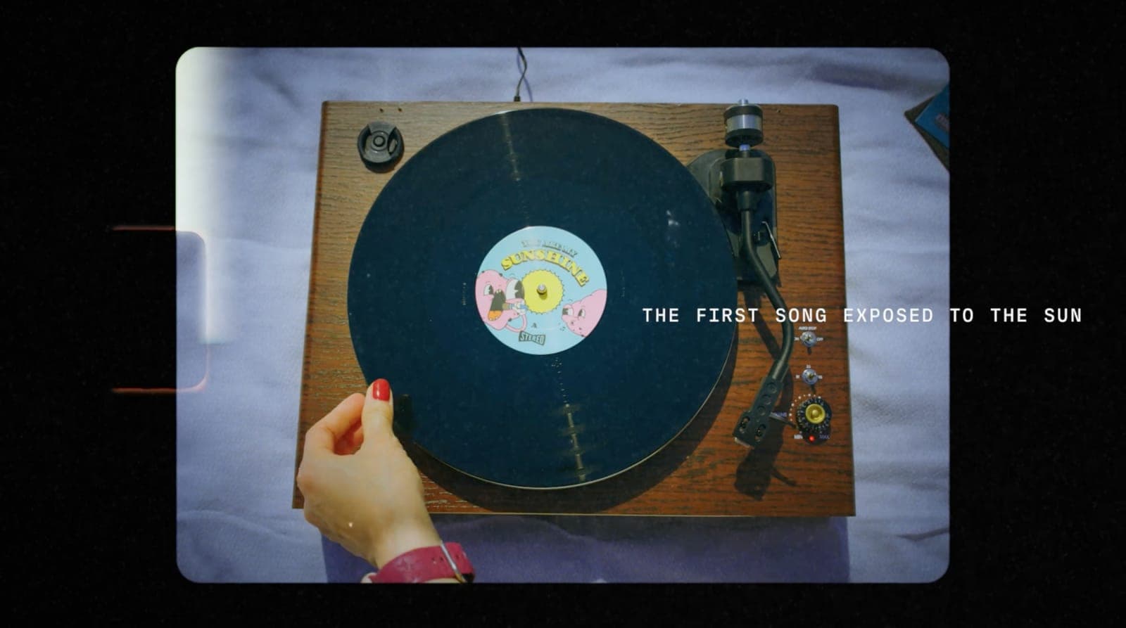 Overhead view of a hand placing the You Are My Sunshine record on a wooden turntable, with the words The first song exposed to the sun